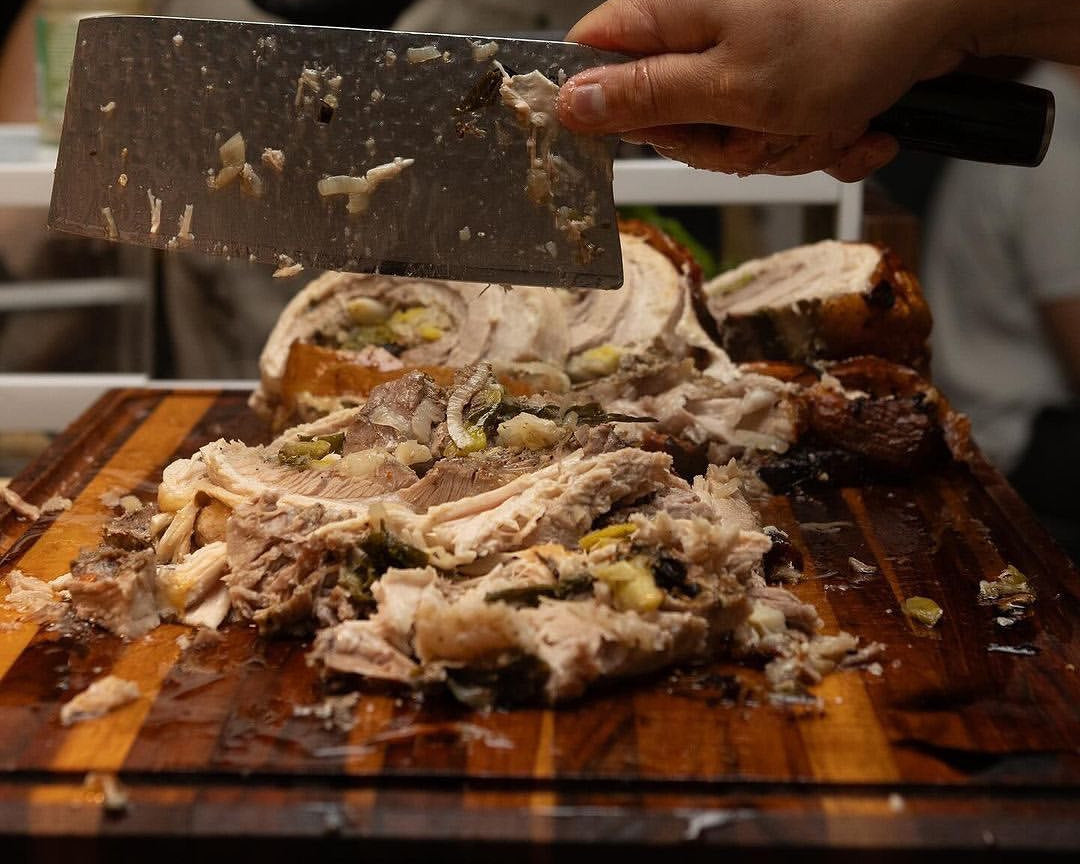Person cutting porchetta on a large teak wood cutting board by Sonder Los Angeles.