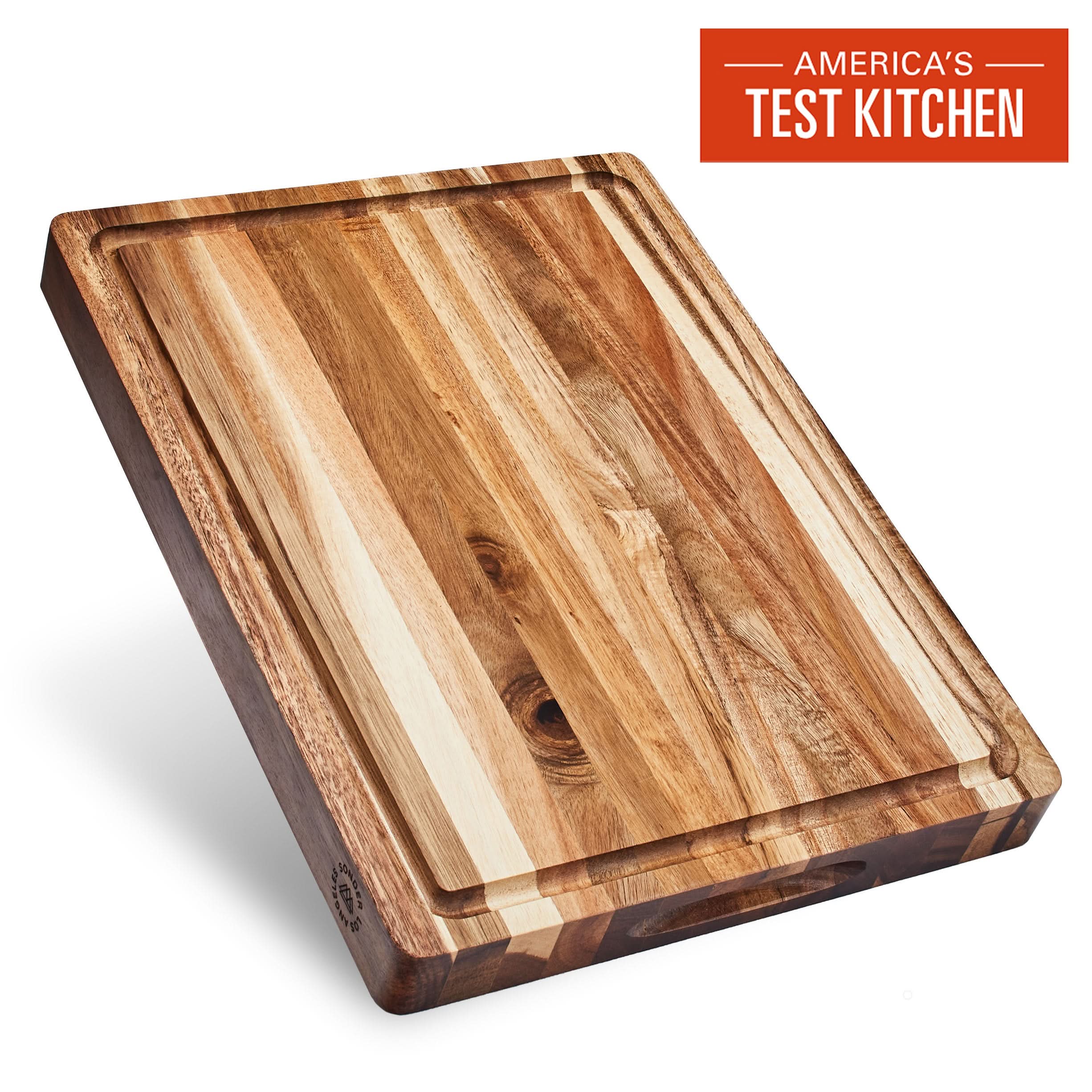 A rectangular acacia wood cutting board with a juice groove, displayed at an angle to show the grain of the wood.