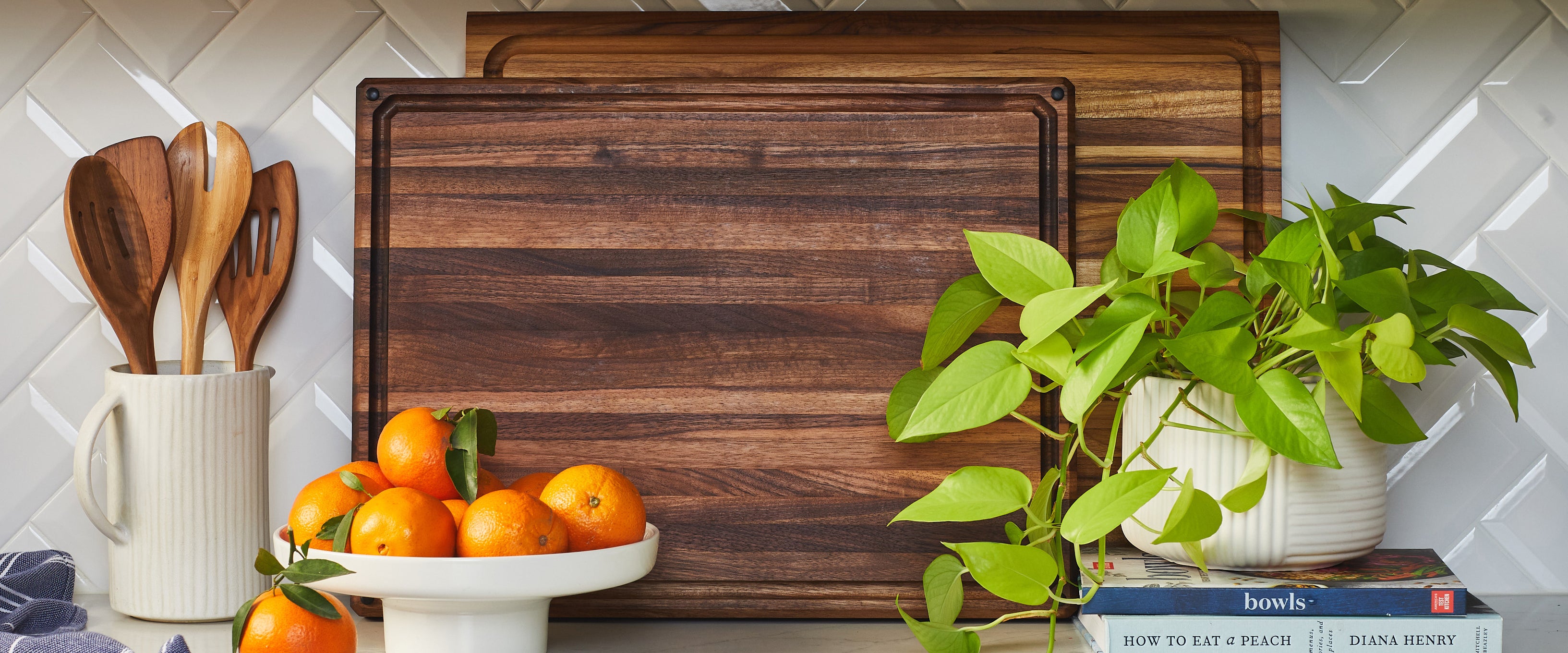 Wooden cutting boards with oranges, utensils, and a plant on a kitchen counter.