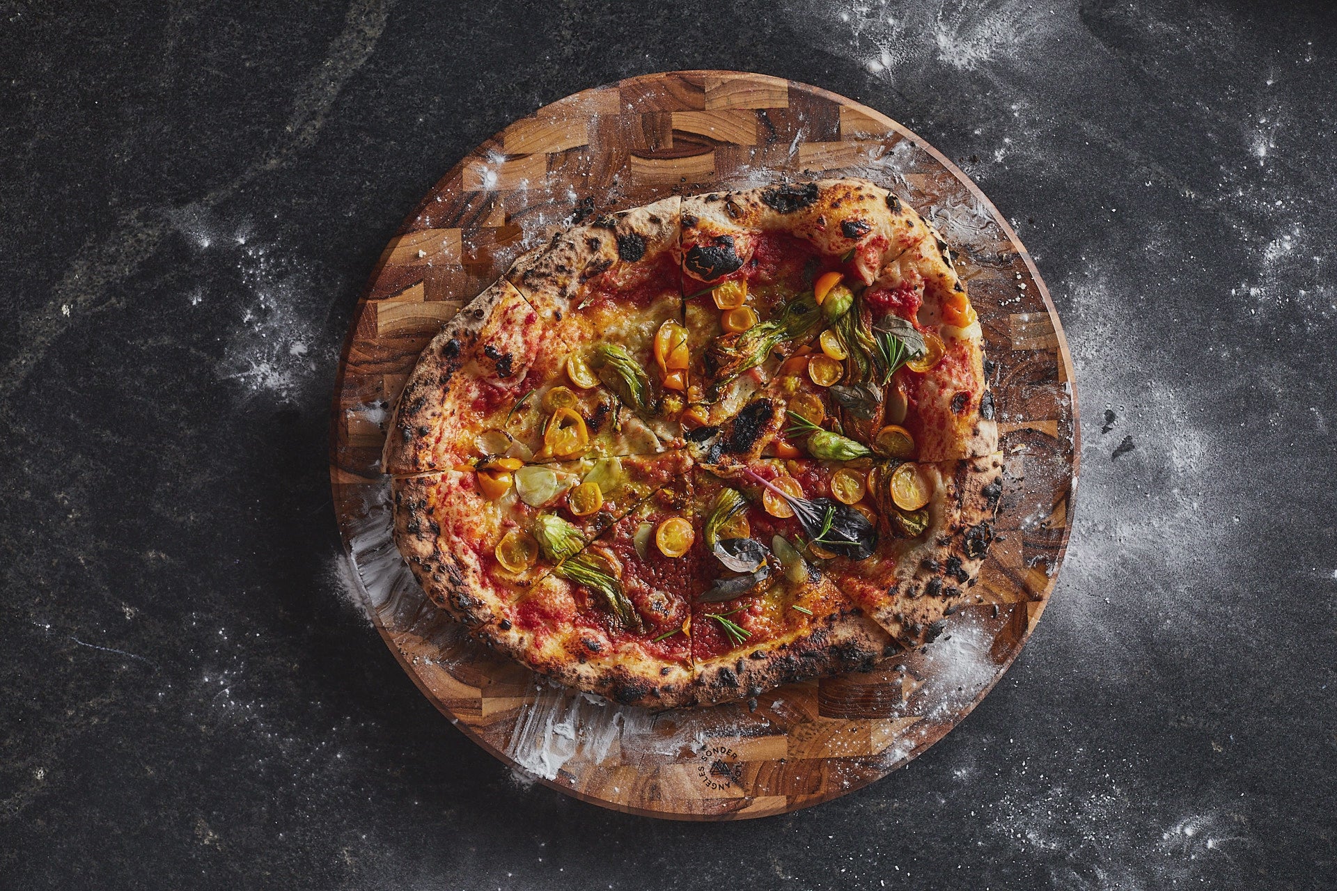 People grabbing slices of pizza off of a circular wood pizza board by Sonder Los Angeles