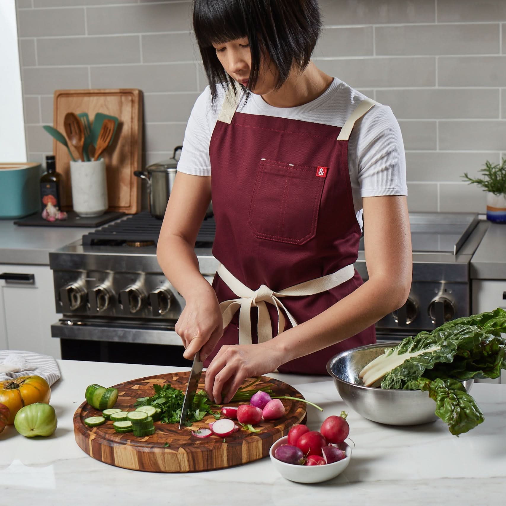Woman cutting parsley in kitchen on round Sonder Los Angeles Vincent End Grain Teak Wood Butcher Block