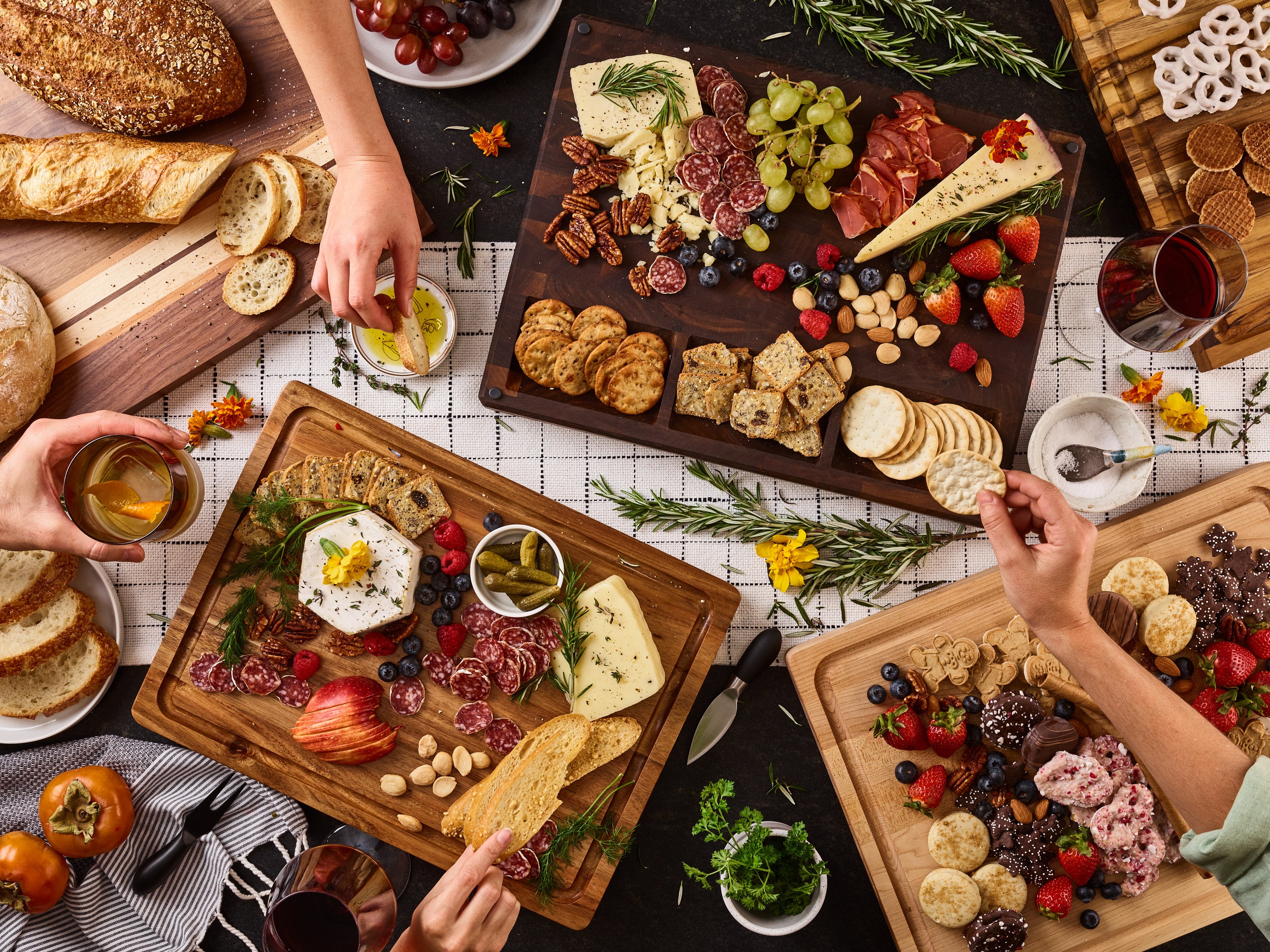 A table covered in full charcuterie boards with hands coming into to take things.