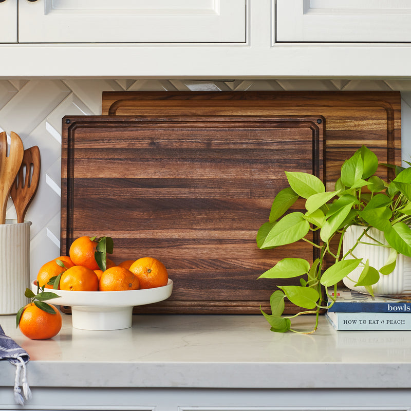 Large edge grain walnut board and extra large teak board displayed in white modern kitchen.