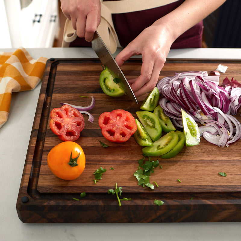 Person slicing tomatoes and onions on a large edge grain walnut cutting board