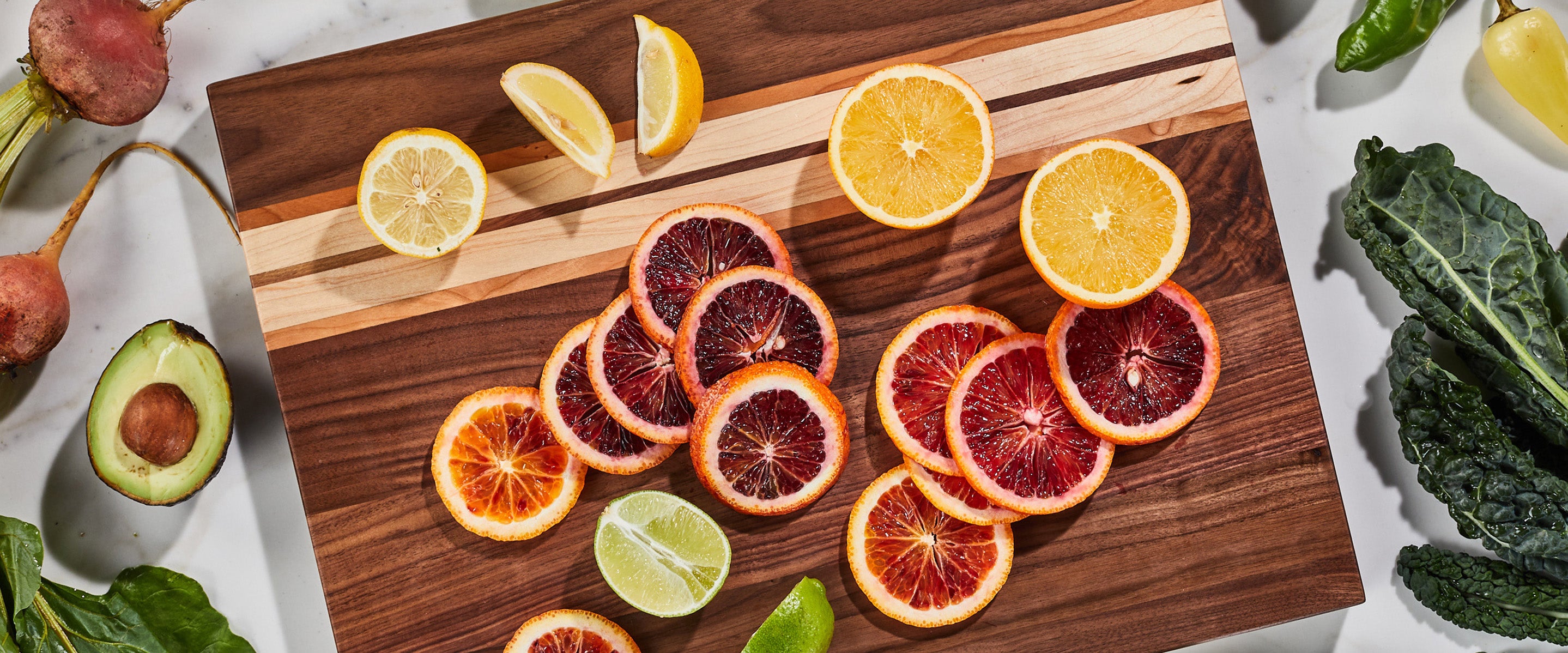 Sliced oranges on a modern walnut wood cutting board with lemons, limes, and avocados.