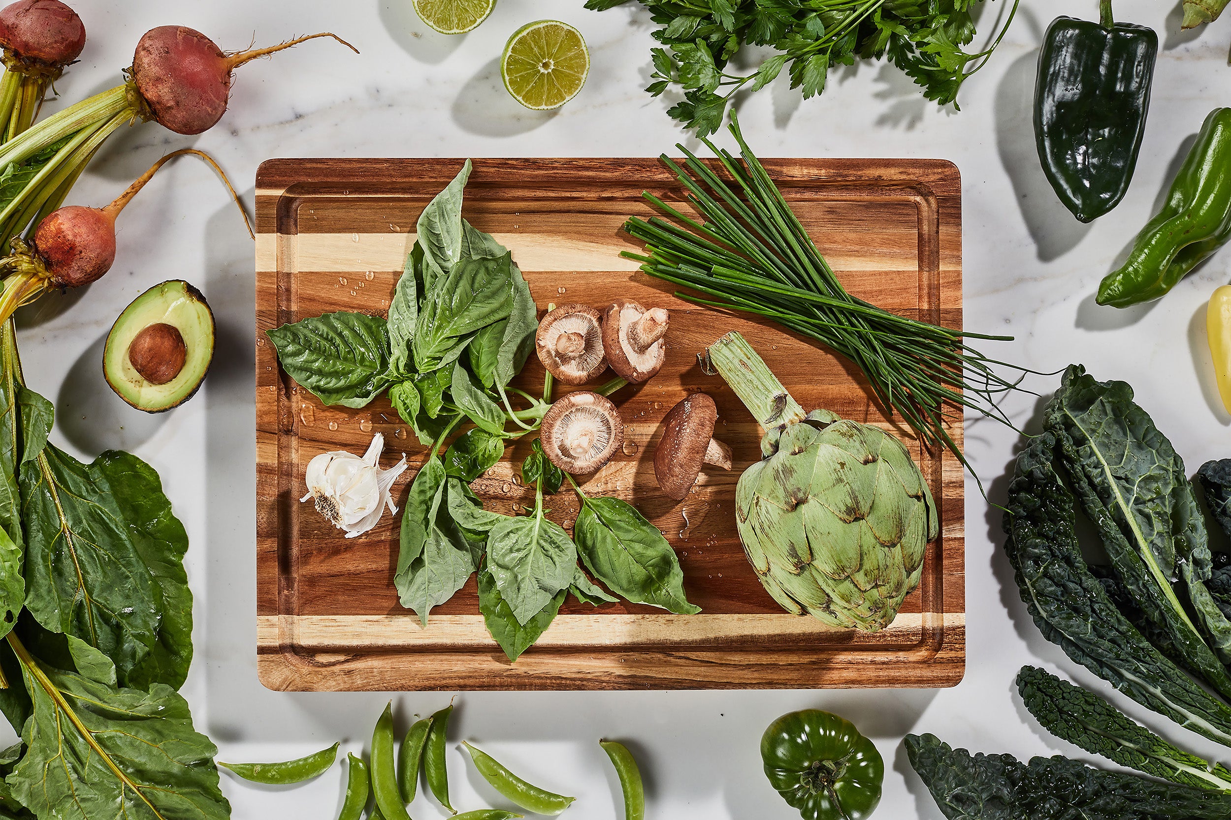 Fresh farmers market produce of leafy greens, avocados, mushrooms, beets, on a beautiful acacia wood cutting board by sonder los angeles