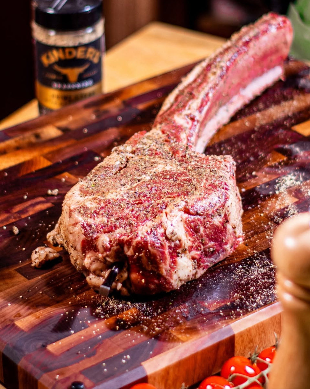 Raw tomahawk steak on a Sonder LA Welton end grain American Black Walnut Cutting Board 20 x 15 with seasoning bottle and pepper grinder.