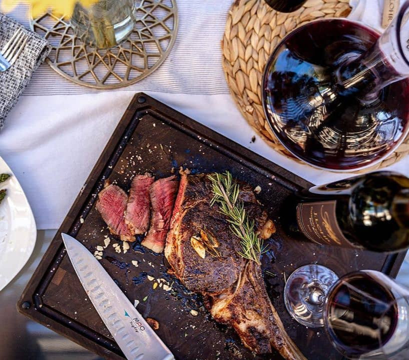 Sliced steak on a pan with asparagus and wine glasses on a table.