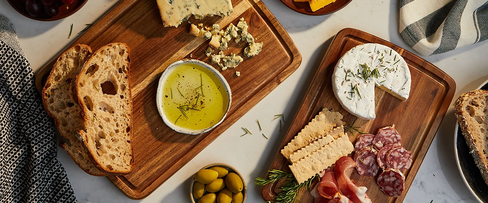 Sonder LA wooden cutting board with bread, olives, and a small bowl of oil on a light background