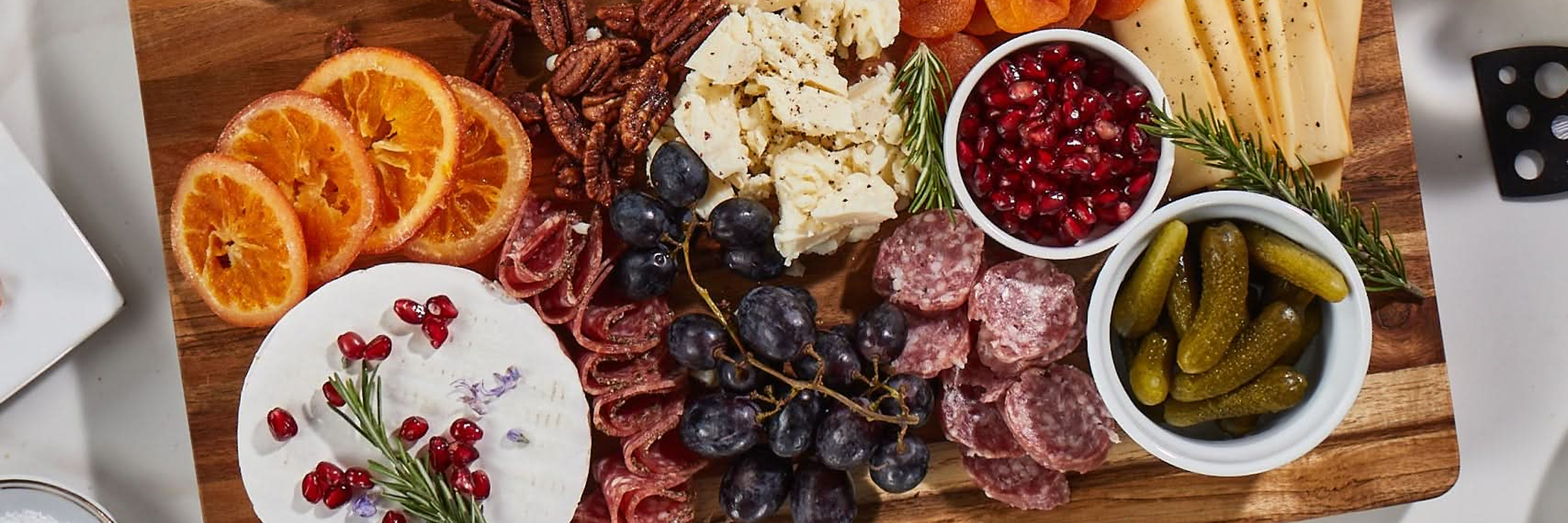 Sonder LA wooden charcuterie board with various meats, cheeses, fruits, and pickles on a white surface.