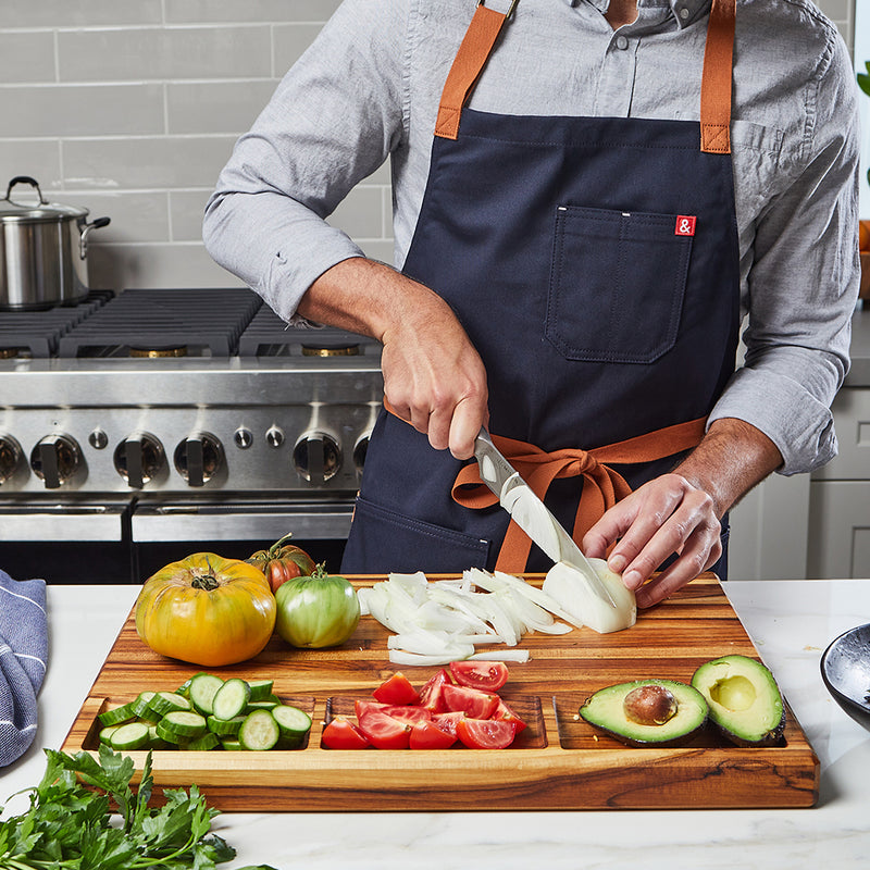 Man in kitchen chopping produce with extra large teak wood cutting board with organizing compartments by Sonder Los Angeles