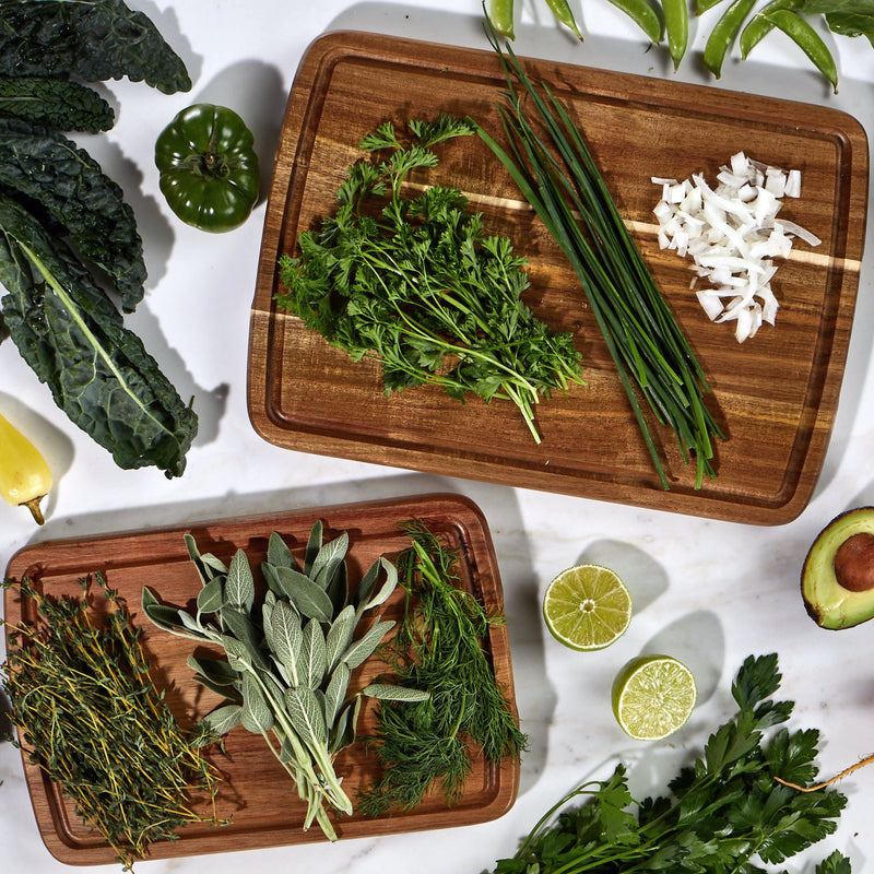 Sonder LA Doheny Duo Small and Medium Acacia Wood Cutting Board Set on a countertop top full of fresh produce and herbs