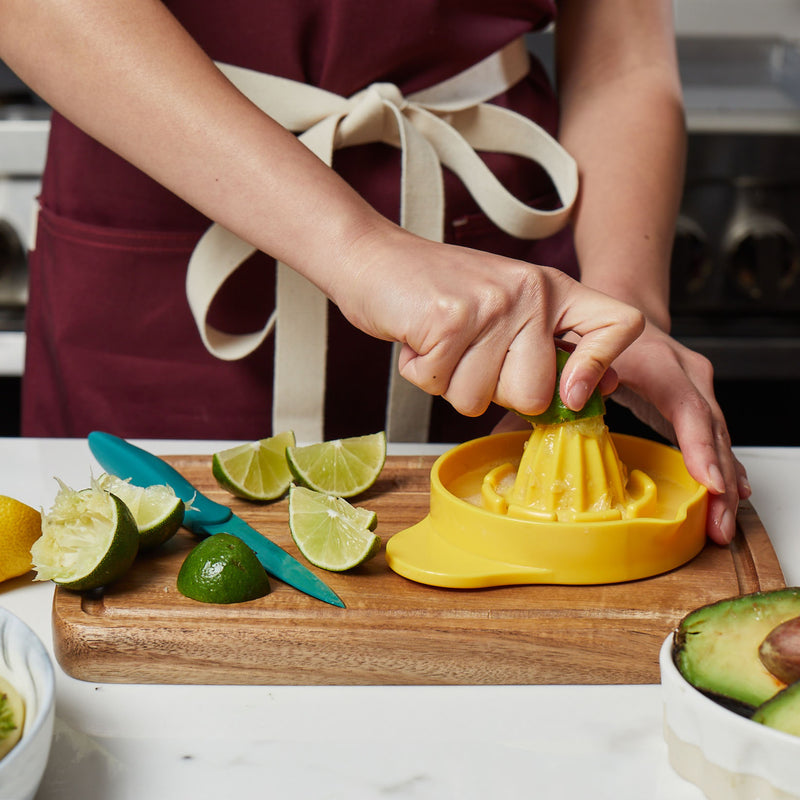 Person slicing and squeezing lime juice on a small wood cutting board with juice groves