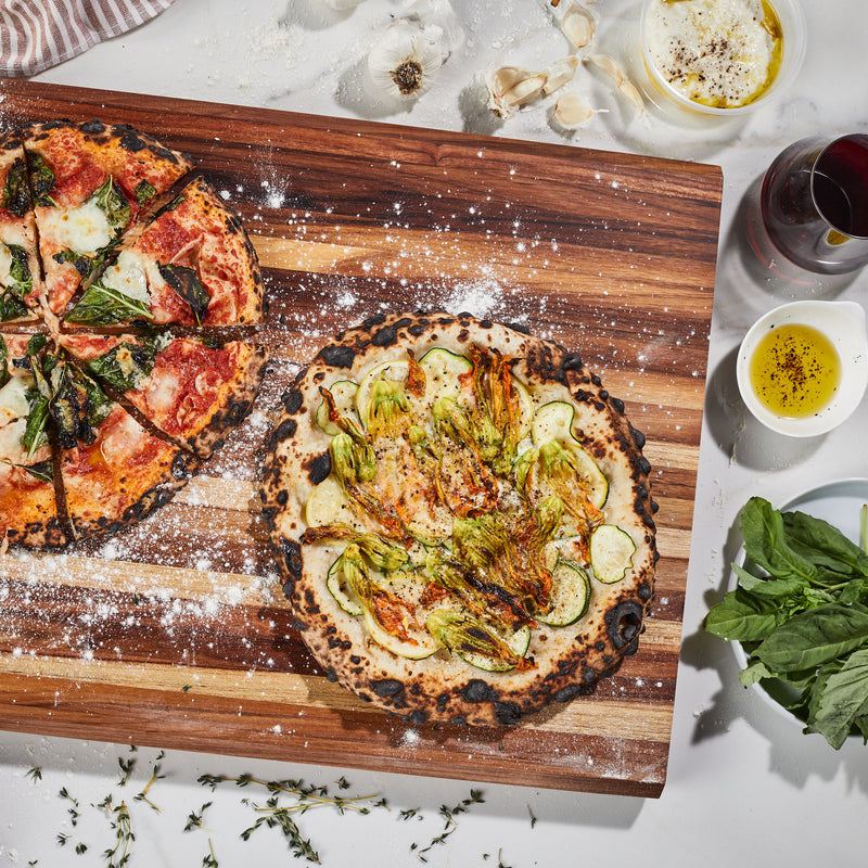 Two home made pizzas on a extra large teak wood cutting board by sonder los angeles