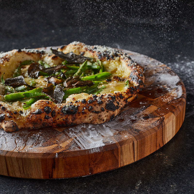 Fresh out of the oven pizza served on a circular thick teak wood cutting board by Sonder Los Angeles