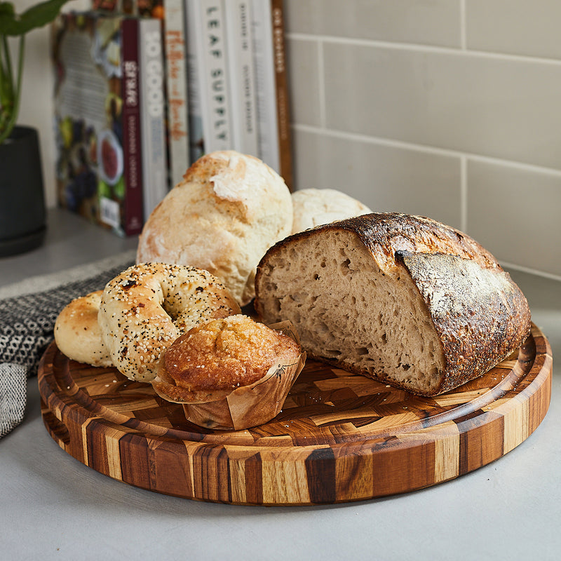 Fresh bread, muffins, bagels on beautiful round end grain teak wood cutting board by Sonder Los Angeles